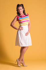 Smiling woman in skirt with hairdo stands in yellow studio, pin up style, full body
