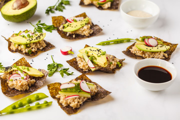 Brown rice, avocado, peas nori wraps with soy sauce and tahini dressing on a white marble background.