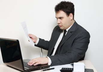 Businessman in suit works with laptop and documents at table with paper, pen, calculator