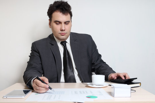 Businessman in suit looks at documents at table with coffee, diagrams, documents, tablet PC