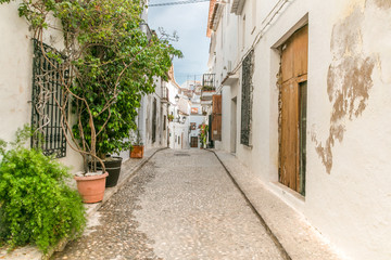 A narrow, quiet stone street in the city of Altea in Valencia, Spain, Costa Blanca. On the sides houses with bright facades and plants in pots.