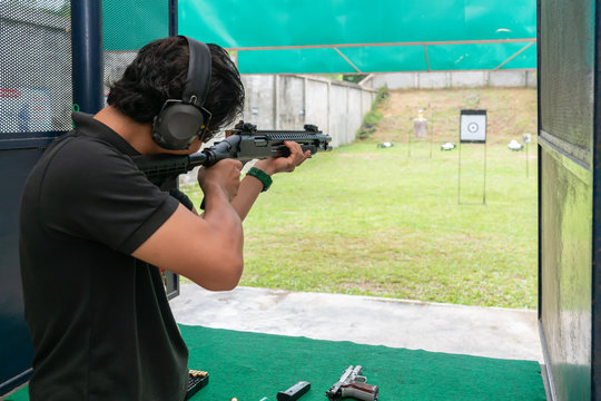 Man wear Ear plug aiming shotgun at Target in Shooting Range. Men Practicing Fire Pistol Shooting.