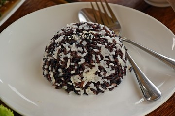  White and black Steamed rice or boiled rice In a white plate placed on a wooden table.