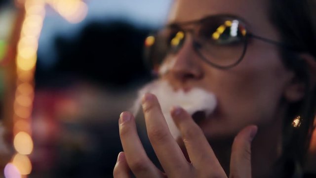 Close up blurred motion of a young beautiful girl in evening amusement park eating cotton candy, pushes it in the mouth