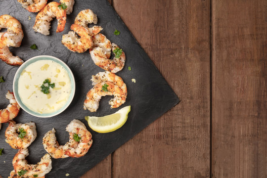 Overhead photo of plate of cooked shrimps on a dark rustic background, with a sauce, with copy space