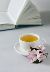 Cup of tea, apple blossom and open book on background