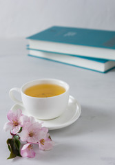 A cup of tea with apple blossom and books in the background