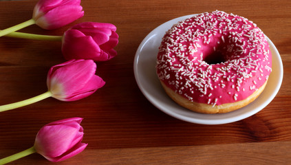 Donut with pink icing and red tulips on a dark wooden background. Top view. Food concept.
