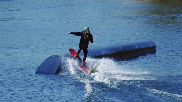 Rider wakeboarding in cable wake park. Speed water sports. Extreme wakeboarding. Wakeboarder surfing along sportive pipe in slow motion. Healthy lifestyle. Extreme water boarder
