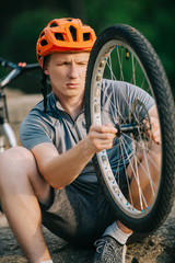 close-up shot of young trial biker examining bike wheel outdoors