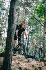 Naklejka premium athletic young trial bikers riding at beautiful pine forest