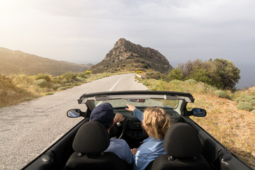 Young couple driving convertible blue rental car without roof on mountain road in Naxos island,...