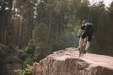 back view of young trial biker riding on rocks outdoors
