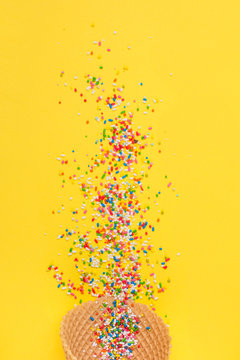 Ice cream cone with colorful sprinkles on yellow background. Closeup, vibrant colors.