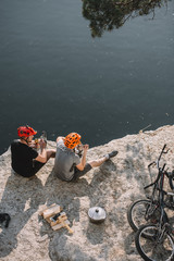 high angle view of bike travellers eating canned food on rocky cliff over lake