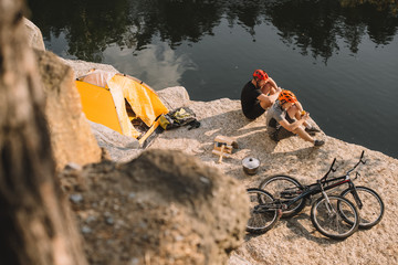 Fototapeta premium high angle view of active trial bikers eating canned food in camping on rocky cliff