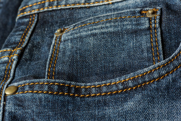 Close-up of a piece of blue jeans with orange stitches. Pocket with rivets close-up.
