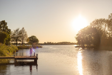 Ein Mädchen tanzt auf einem Bootssteg an einem See im Sonnenuntergang