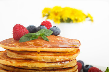 Stack of pancakes decorated with bluberries, raspberries and mint leaves. Yellow flowers in background