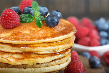 Closeup of homemade american pancakes, with fresh blueberries, raspberries and maple syrup on a rustic wooden  background