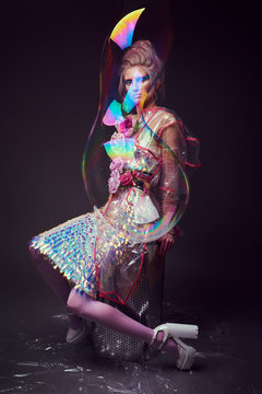 Gorgeous woman in biofuture pompadour style. Female in fashion transparent raincoat with splendid make up and hairstyle, photoshoot through soap bubble