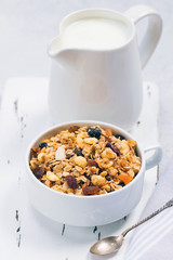 Cup of muesli with tropical fruits and white milk jug on wooden board. Concept of healthy eating in pure tones.