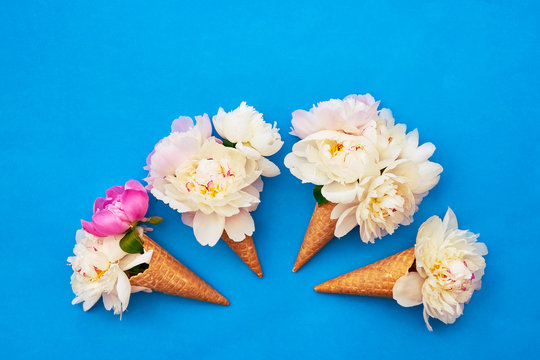 Waffle ice cream cone with white peony flowers on blue background. Summer concept. Copy space, top view.