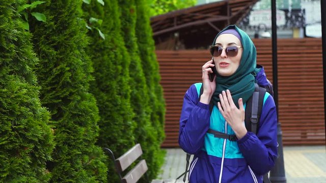 portrait of a girl tourist in a headscarf and sunglasses with a backpack talking on the phone