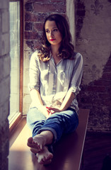 Fototapeta premium Young cute girl meditates on the window. Young beautiful woman is sitting on the window. Thoughtful look. Concept sadness. Concept emotions