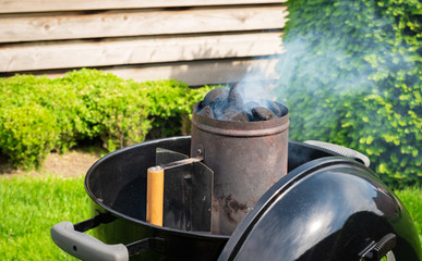 Smoking charcoal briquettes in a chimney starter prepared for a garden barbecue party.