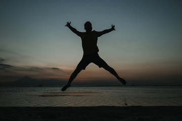 .Young man on vacation in the Gili Islands enjoying a colorful sunset in Indonesia. Jumping for the picture. Photograph and vacation.