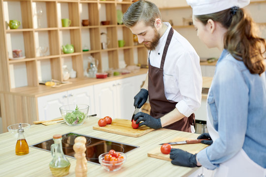 Portrait of professional cook working in restaurant kitchen with su-chef, both cutting vegetables standing at wooden workstation, copy space