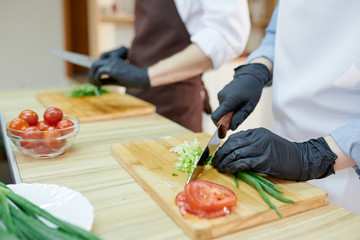 Closeup of unrecognizable female chef cutting vegetables standing at wooden table in restaurant kitchen, copy space