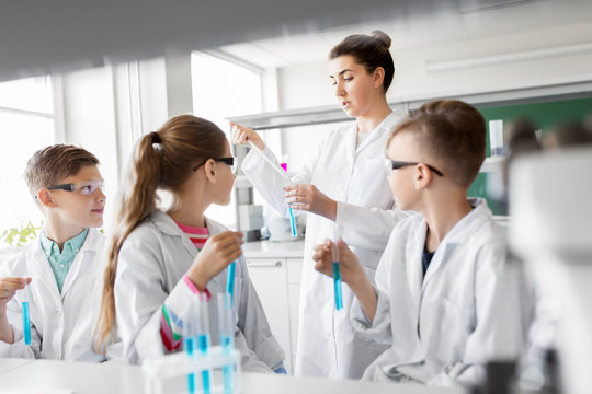 education, science and children concept - teacher and kids or students with test tubes studying chemistry at school laboratory