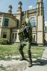 Young male military soldier with a rifle near the old building