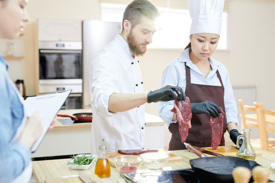 Team of professional chefs working in modern restaurant kitchen standing round wooden table and cooking meat together, copy space