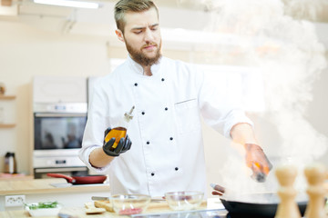 Portrait of handsome  professional chef working in modern restaurant kitchen standing at wooden table and cooking delicious dishes, copy space