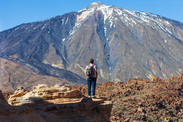 Fototapeta premium Back view of traveler man standing on the edge of rock looking to volcano El Teide