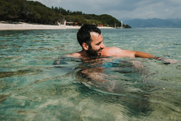 .Handsome man on vacation in the gili islands enjoying at the lonely beach with turquoise blue water, relaxing, sunbathing and playing in the water. Travel photography.
