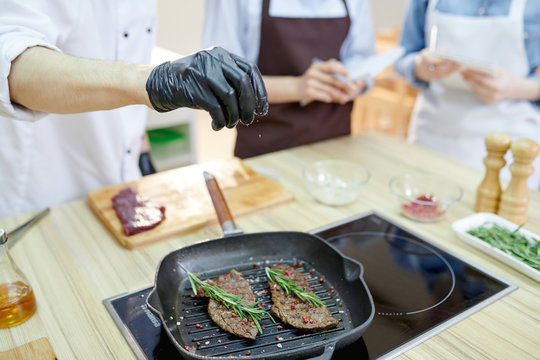 Closeup of unrecognizable professional chef cooking meat on frying pan while cooking in modern restaurant kitchen, copy space