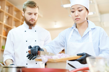 Obraz premium Portrait of focused female Asian chef cooking delicious dishes while working in modern restaurant kitchen with su-chef, copy space