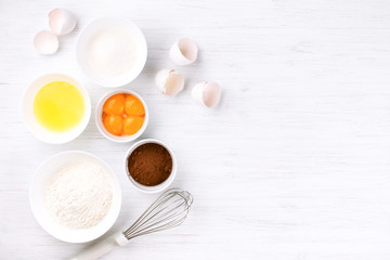 Fototapeta na wymiar Ingredients for baking sponge cake. Eggs, flour, sugar, cacao and whisk. Top view