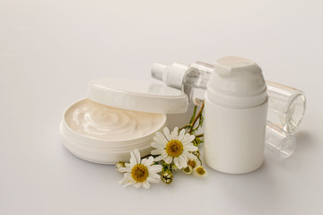         Natural cosmetics for face and body skin care. A round jar with cream, a bottle with lotion and fresh chamomile flowers on a light wooden background. 