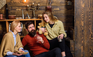 Family of bookworms reading together on couch. Parents and teenage daughter spending Christmas in countryside. Bearded man drinking mulled wine on winter evening. Curious girl looking at her dad