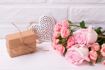 Pink roses flowers, decorative heart  and  wrapped box with present on white wooden background.