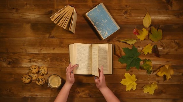Autumn concept top view. Books, maple leaves, tea on the old wooden table. Woman writing notes in the notebook