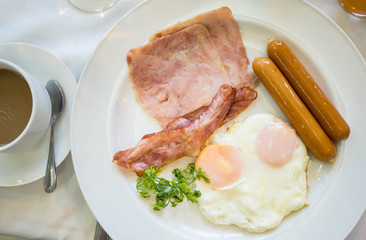 American breakfast with sunny side up eggs,ham, bacon, coffee and juice, and salad on the table ,top view