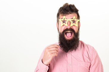 Superstar concept. Man holds party props star shaped eyeglasses, white background. Hipster with beard and mustache on cheerful surprised face posing with star shaped glasses, copy space