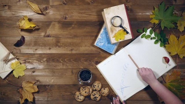 Autumn concept top view. Books, maple leaves, tea on the old wooden table. Woman writing notes in the notebook