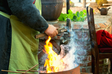 Close-up of blacksmith manually forging the molten metal on the anvil in smithy workshop.